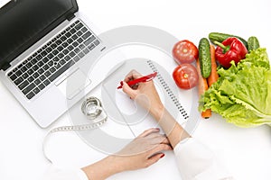 Vegetable diet nutrition or medicaments concept. Doctors hands writing diet plan, ripe vegetable composition, laptop and measuring photo