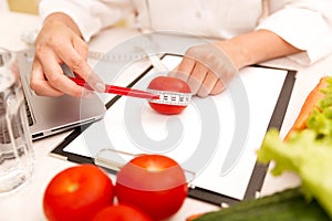 Vegetable diet nutrition or medicaments concept. Female nutrition doctor with vegetables and measuring tape on table photo
