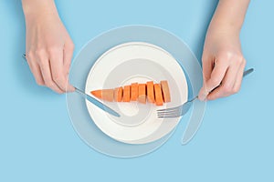 Vegetable diet and raw food. Female hands with a fork and a table knife over a plate of raw carrots