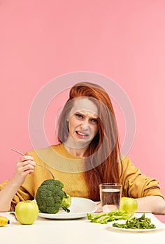 Vegetable diet. Sad dull woman holding broccoli on fork while making grimace