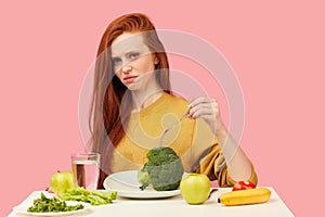 Vegetable diet. Sad dull woman holding broccoli on fork while making grimace