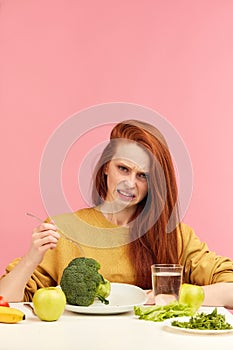 Vegetable diet. Sad dull woman holding broccoli on fork while making grimace