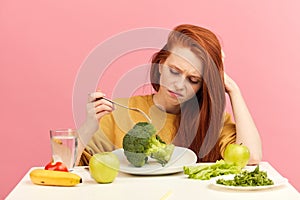 Vegetable diet. Sad dull woman holding broccoli on fork while making grimace