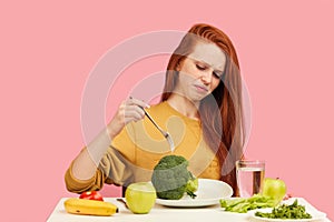 Vegetable diet. Sad dull woman holding broccoli on fork while making grimace