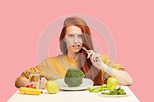 Vegetable diet. Sad dull woman holding broccoli on fork while making grimace