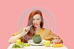 Vegetable diet. Sad dull woman holding broccoli on fork while making grimace