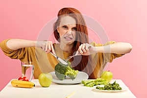 Vegetable diet. Sad dull woman holding broccoli on fork while making grimace