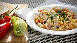 Vegetable dish called lecho containing peppers, tomatoes, onion, eggs and tofu served on white plate with chopped chives and