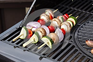 Vegetable kebabs, with courgette, red onion, red pepper, mushroom and tomato, cooking on a gas barbecue