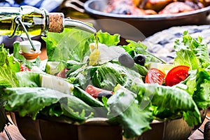 Vegetable lettuce salad. Olive oil pouring into bowl of salad. Italian Mediterranean or Greek cuisine. Vegetarian vegan food