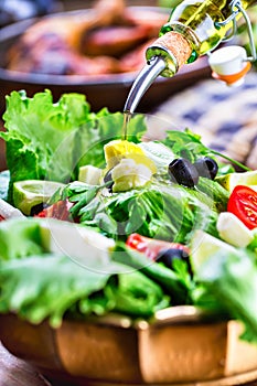 Vegetable lettuce salad. Olive oil pouring into bowl of salad. Italian Mediterranean or Greek cuisine. Vegetarian vegan food