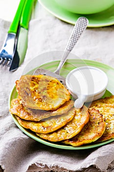 Vegetable marrows fritters with sour cream on a green plate.