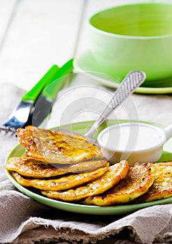 Vegetable marrows fritters with sour cream on a green plate.