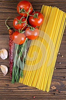 Vegetable pasta ingredients: spaghetti, peppers, tomatoes, basil, rosemary, olive oil, garlic, sea salt and spices on a dark