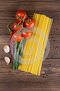 Vegetable pasta ingredients: spaghetti, peppers, tomatoes, basil, rosemary, olive oil, garlic, sea salt and spices on a dark