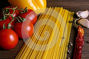 Vegetable pasta ingredients: spaghetti, peppers, tomatoes, basil, rosemary, olive oil, garlic, sea salt and spices on a dark