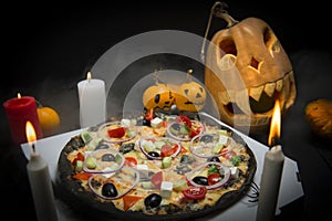 Vegetable pizza in Halloween decorations: pumpkins with painted faces, Lights of burning candles In horror fog with jack o lantern