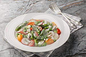 Vegetable salad of asparagus, fresh radishes, cherry tomatoes, green peas and goat cheese close-up in a plate. Horizontal