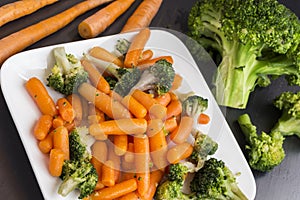 Vegetable salad: broccoli and carrots in a white plate on a black background