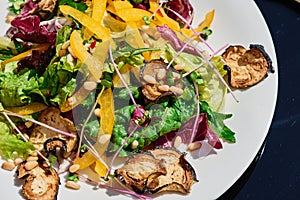Vegetable salad with fresh greens and grilled vegetables on a glass dark table on the summer terrace