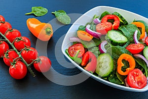 Vegetable salad of fresh tomato, cucumber, onion, spinach and pepper in a bowl.