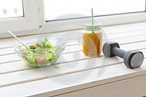 Vegetable salad fruit smoothies and dumbbell lie on a white windowsill. Concept of healthy lifestyle physical activity