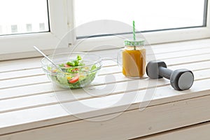 Vegetable salad and fruit smoothies and dumbbell lie on a white windowsill. Concept of healthy lifestyle physical