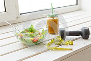 Vegetable salad and fruit smoothies and dumbbell lie on a white windowsill. Concept of healthy lifestyle physical