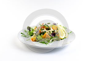 Vegetable salad with greens and pumpkin on a white plate on an isolated background, bright summer vegetables