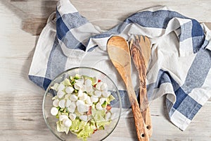 Vegetable salad with mozzarella on a white-blue towel next to spoons of olive