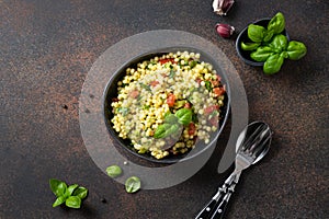 Vegetable salad with pasta ptitim or Birdy, Israeli couscous decorated basil leaves on dark. Top view