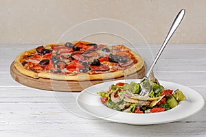 Vegetable salad with roasted meat and cheese and Sliced whole salami pepperoni pizza on a wooden table.