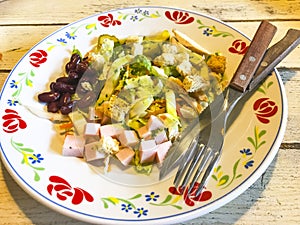 Vegetable salad with sausage and beans in plate on old wooden table.