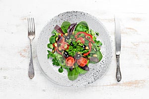 Vegetable salad with spinach, tomatoes, paprika and pumpkin seeds in a plate on a wooden background Top view.