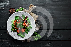 Vegetable salad with spinach, tomatoes, paprika and pumpkin seeds in a plate on a wooden background Top view.