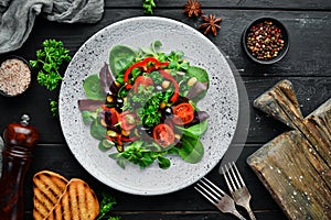 Vegetable salad with spinach, tomatoes, paprika and pumpkin seeds in a plate on a wooden background Top view.