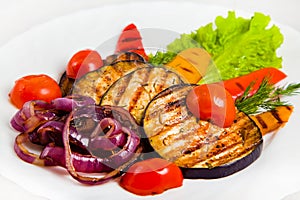 Vegetable salad on white plate with grilled eggplant, cherry tomatoes, red and yellow bell peppers, purple onions, dill