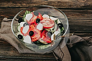 Vegetable salad on a wooden background. Lettuce, tomato, cucumber, olives, mozzarella and olive oil. Wholesome healthy