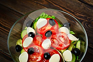 Vegetable salad on a wooden background. Lettuce, tomato, cucumber, olives, mozzarella and olive oil. Wholesome healthy food