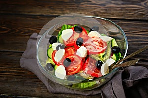 Vegetable salad on a wooden background. Lettuce, tomato, cucumber, olives, mozzarella and olive oil. Wholesome healthy food