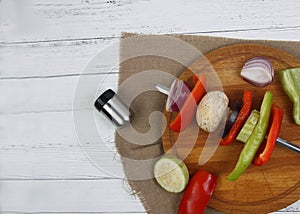 Vegetable shashlick on spitter on cutting board and salt shaker on white vooden background flat lay