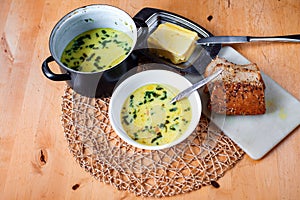 Vegetable soup in bowl and pot, bread, butter on kitchen table