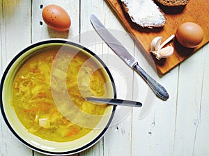 vegetable soup, bread and butter, eggs, a cup of tea and garlic on the table