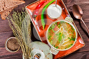 Vegetable soup, broth with noodles, herbs, parsley and vegetables in bowl with sour cream, spice, pepper, dried thyme and bread