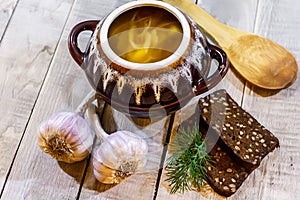 Vegetable soup in a pot with bread and fresh garlic on a gray wooden background