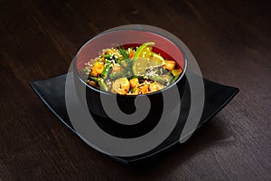 Vegetable wok with prawns in black round bowl on brown wooden background