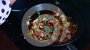 Vegetables added to chicken chorizo while cooking in frying pan on hob at home. womens hands