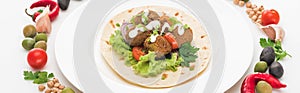 Vegetables arranged in round frame around falafel on pita on plate on white background, panoramic shot.