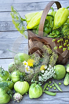 Vegetables in the basket. A wicker basket with tomatoes, peppers, dill and a bouquet of wild flowers stands on a wooden background