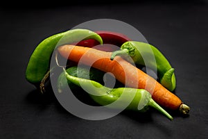 Vegetables on a black background. Carrot, green pepper, red pepper and cucumber